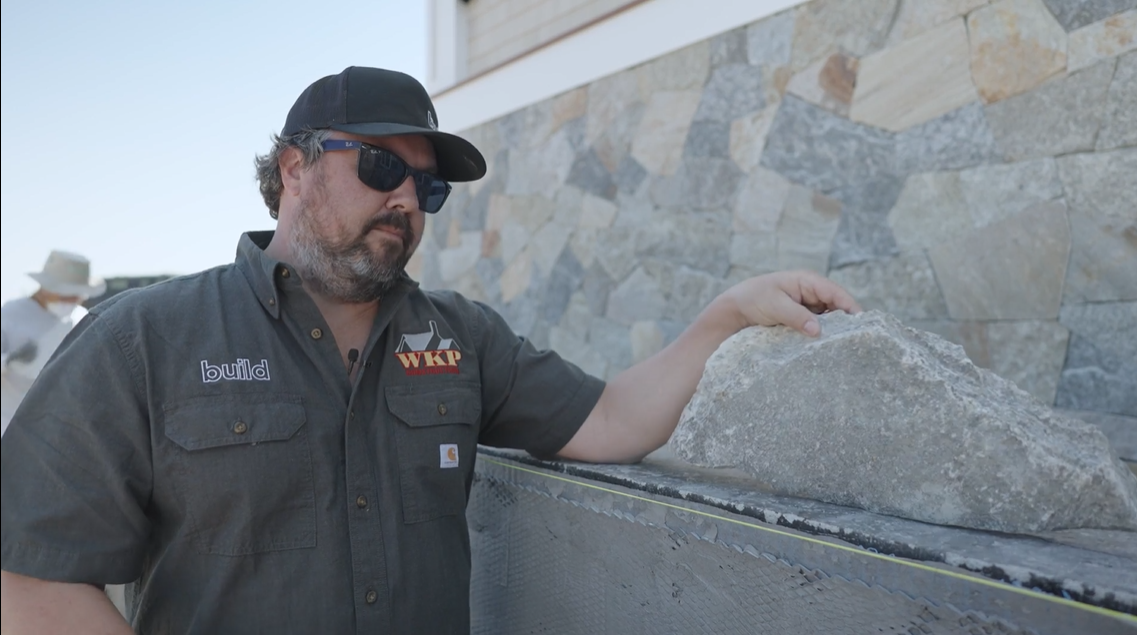 Man standing with stone veneer in front of home.