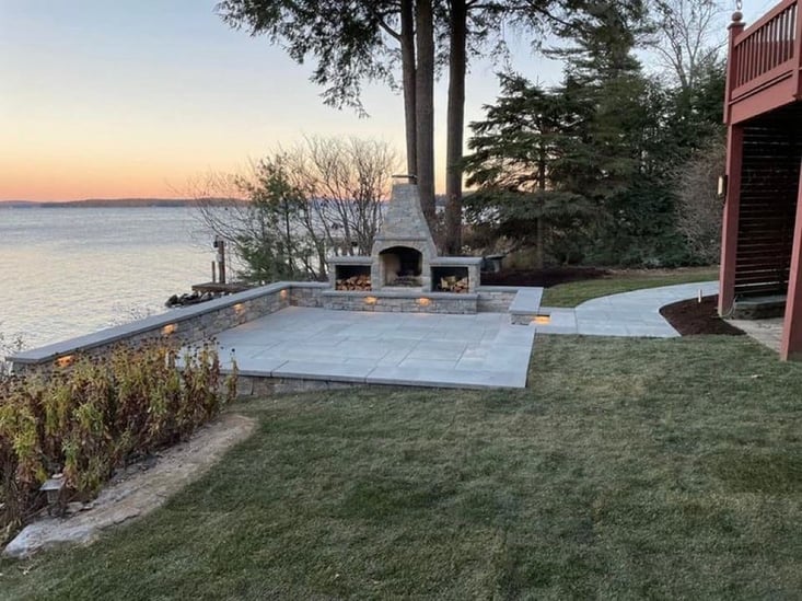 Outdoor space with patio and natural stone fireplace by the water.